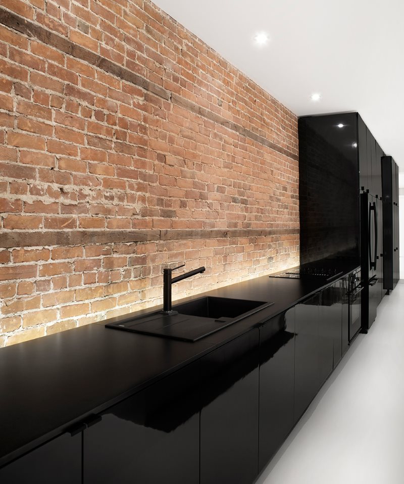 Черный глянцевый гарнитур вдоль кирпичной стены кухни