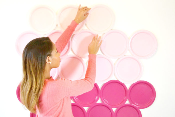 A woman putting pink paper plates on a wall