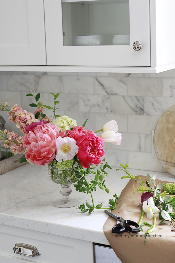 DIY floral centerpiece with pink peonies, tulips, and greenery in a white kitchen. 