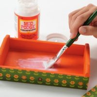 Painting Mod Podge Gloss inside of a painted wood tray with a green handled paint brush