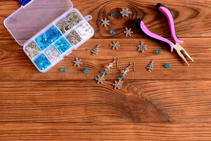 Handmade female chandelier earrings. Beautiful earrings made of blue and white beads and metal snowflakes. Pliers, box of craft materials on a wooden table stock image
