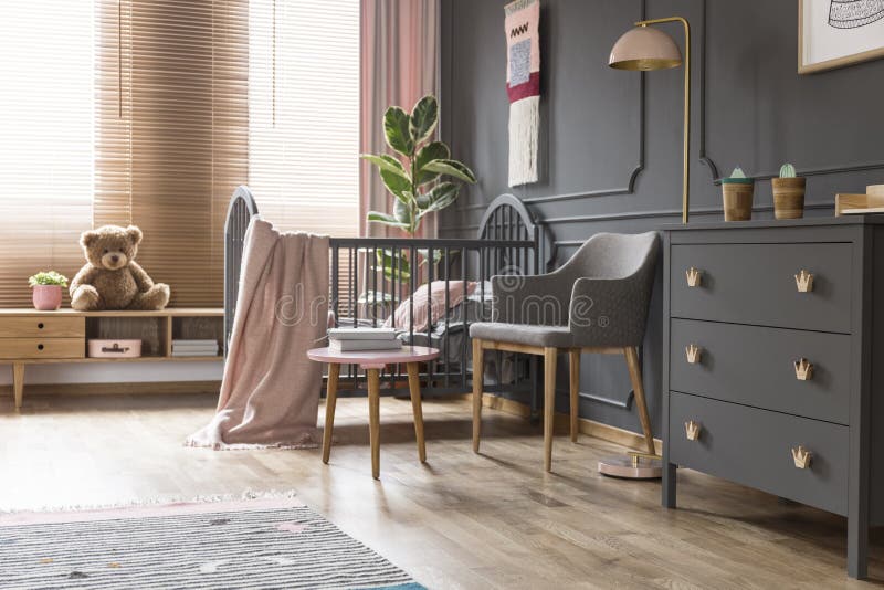 Real photo of a cot standing next to an armchair, lamp and cupboard in dark and classic baby room interior stock photos